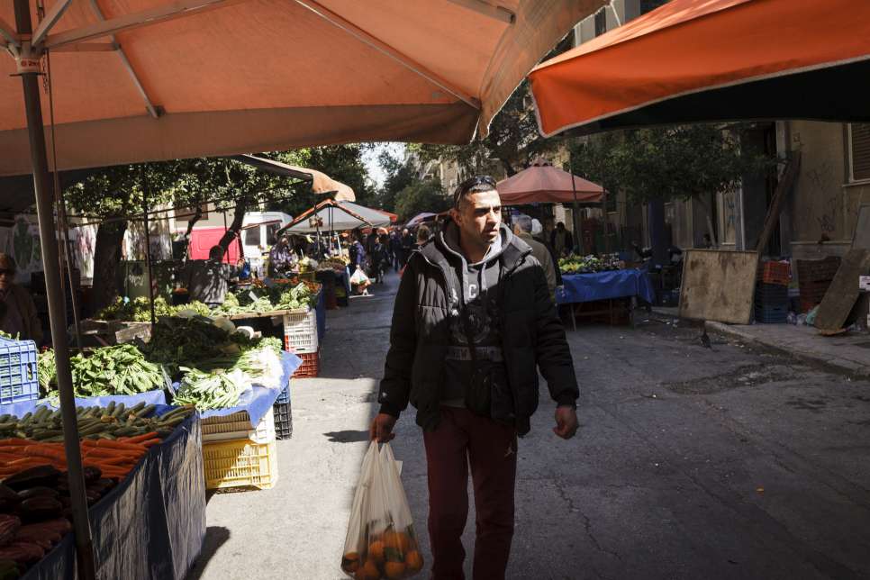 Ibrahim walks past street vendors selling fruit and vegetables at a market near his home in Athens.