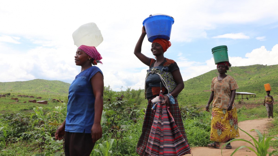Aïcha (devant) rentre chez elle avec d'autres femmes après avoir puisé de l'eau dans un forage de l'installation de Mulongwe, en République démocratique du Congo. 