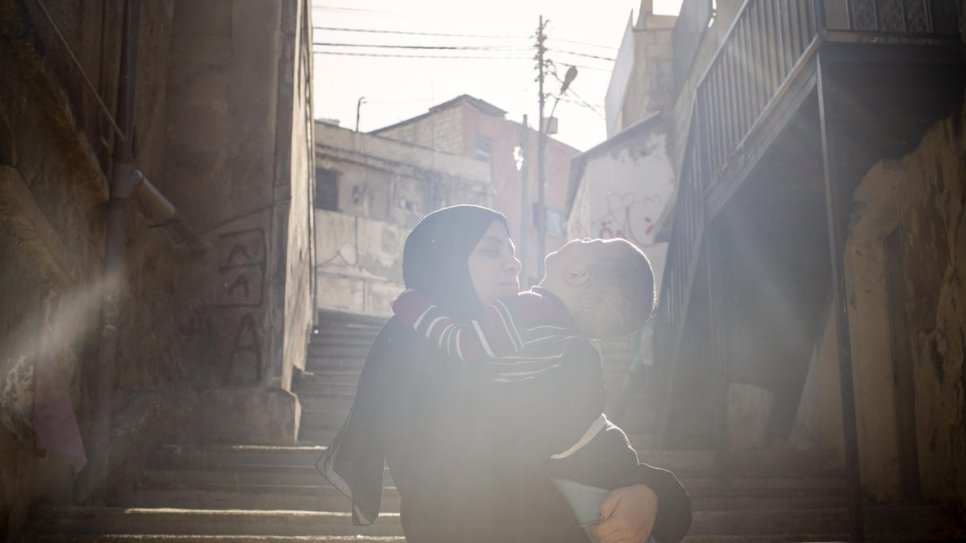Fatima tient son plus jeune fils, Ibrahim, dans ses bras devant leur maison à Amman, en Jordanie. 