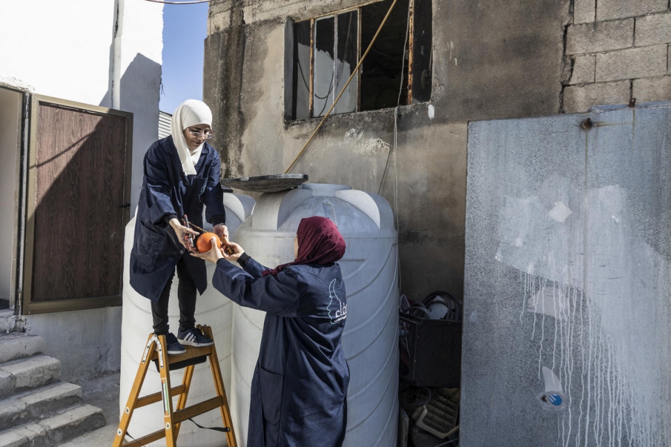 المتدربة واللاجئة السورية بثينة تساعد صفاء في تركيب خزان للمياه في إربد، الأردن. 
