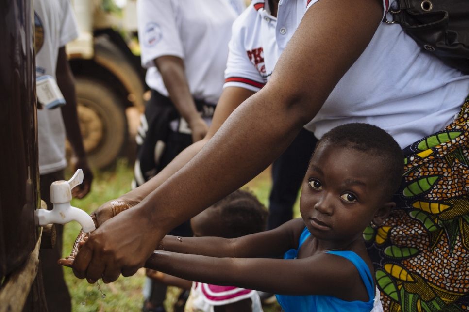 A young girl is helped by her mother to wash her hands as they and other refugees queue to have their temperature recorded in an effort to combat the transmission of the Ebola Virus Disease, at a border post near the Cavalla River, which demarcates the border with Côte d'Ivoire, in Maryland, Liberia.