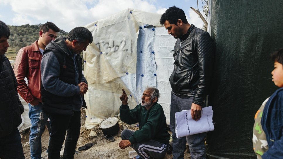 Sardar (centre-left) speaks with Abdul What Qadiri (sitting), a 65-year-old Afghan asylum-seeker who has cancer, at the Moria reception and identification centre on Lesvos.