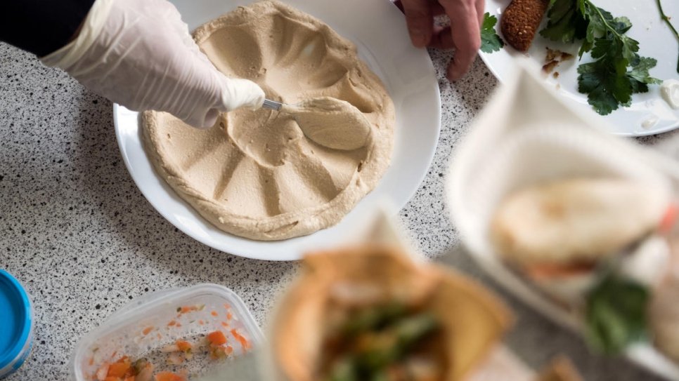 Syrian refugee Fadi Zaim, 32, prepares a plate of hummus in his mother Salma Al Armarchi's kitchen in Berlin, from where she runs her company, Jasmin Catering.