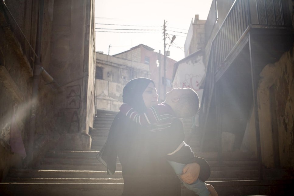 فاطمة تحمل ابنها الأصغر، إبراهيم، خارج منزلهما في عمّان، الأردن.