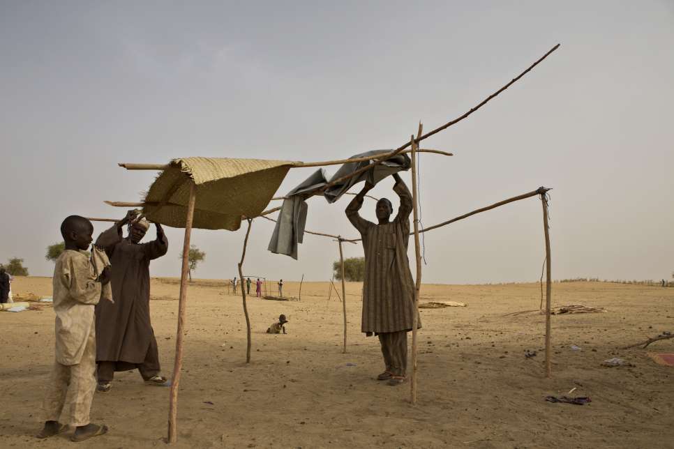 Mahamadou et Bala, avec l'aide d'un des fils de Bala, construisent un abri, au camp de réfugiés du sud du Niger. 