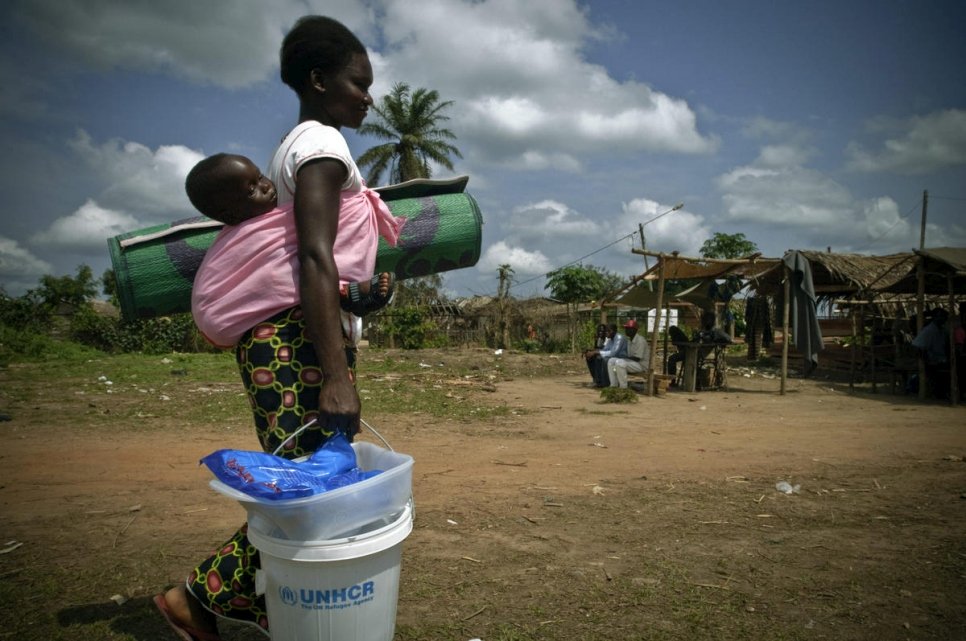 Une réfugiée porte son enfant ainsi que des articles de secours au Congo. 
