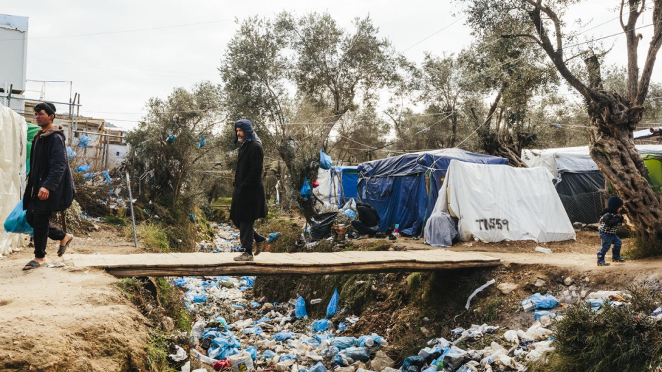 Un homme traverse un ruisseau asséché rempli d'immondices dans un camp de fortune qui jouxte le centre de réception et d'identification de Moria, sur l'île grecque de Lesbos.