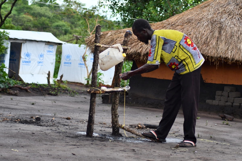 Chris, un réfugié sud-soudanais, utilise son point d'eau avec un robinet à bascule fait de bois, d'un vieux jerrycan et de corde, dans l'installation de Bele, en République démocratique du Congo. 