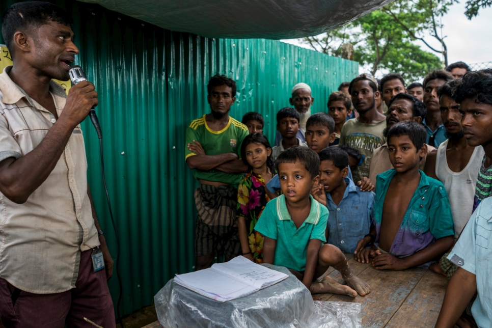 متطوع يستخدم مكبر الصوت لإيجاد عائلة فتى في الرابعة من العمر (الوسط) في مقصورة مخصصة لتوفير المعلومات ممولة من المفوضية في مخيم كوتوبالونغ للاجئين في بنغلاديش.