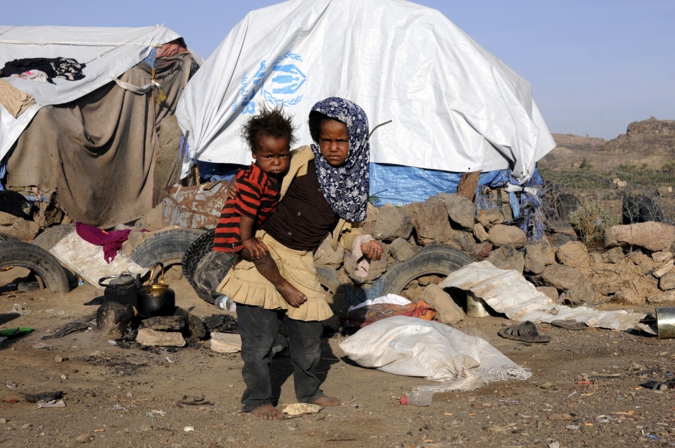 Une petite fille porte son frère devant leur tente dans l'installation de Dharawan, au Yémen. 