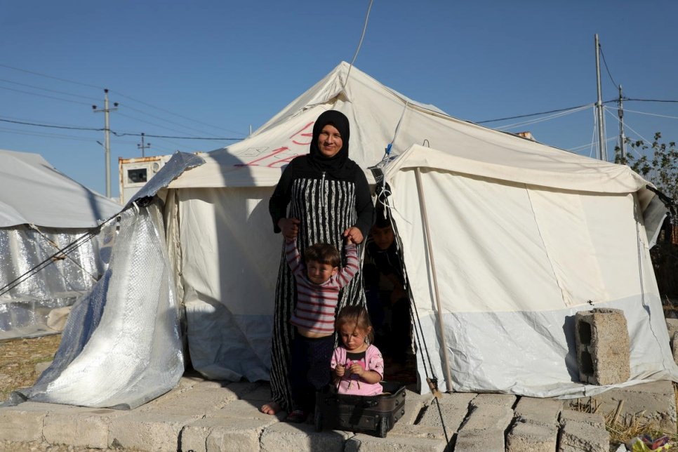 Nadira, une réfugiée syrienne, se tient au soleil devant sa tente familiale dans le camp de Bardarash, gouvernorat de Dohouk, avec son fils de trois ans et sa fille de quatre ans. Leur fuite depuis la Syrie a été très difficile et aujourd'hui Nadira craint l'hiver qui s'annonce.