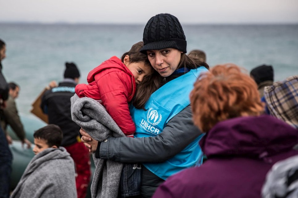 Une employée du HCR tient dans ses bras un jeune enfant réfugié entouré d'une couverture, après avoir été débarqué d'un bateau arrivé dans l'île grecque de Lesbos. Photo d'archives, janvier 2016. 