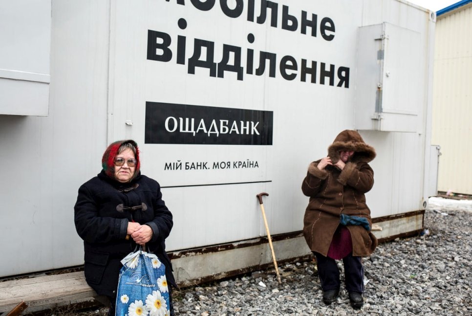 Nelia (à g.) a patienté pendant des heures à côté de cette agence bancaire mobile au point de contrôle de Novotroitske.  