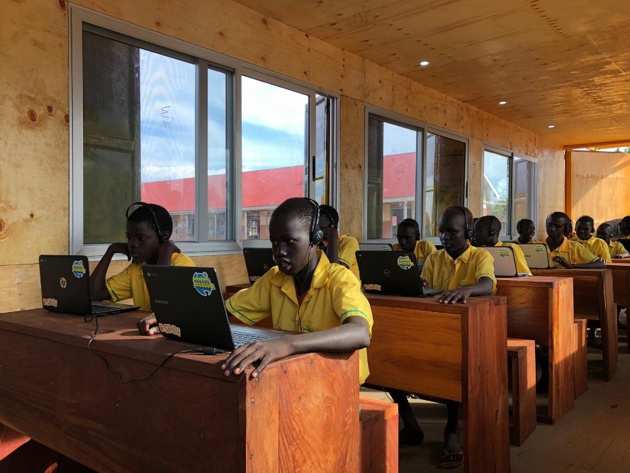 Children sitting at their desks in a classroom with headphones and computers