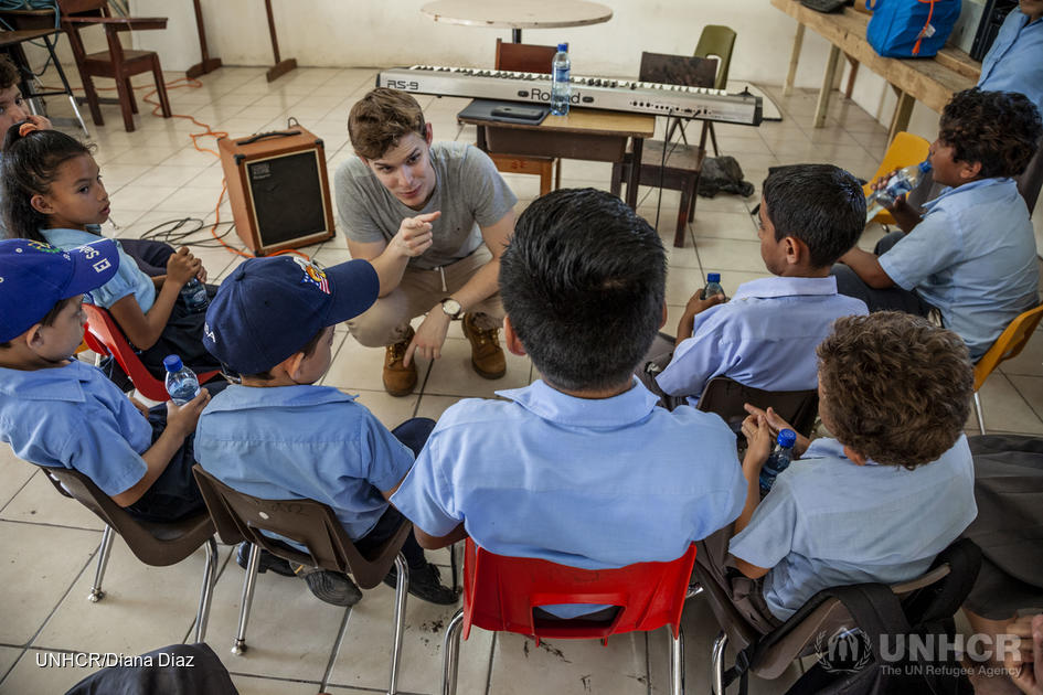 A group of children sit around their music teacher.