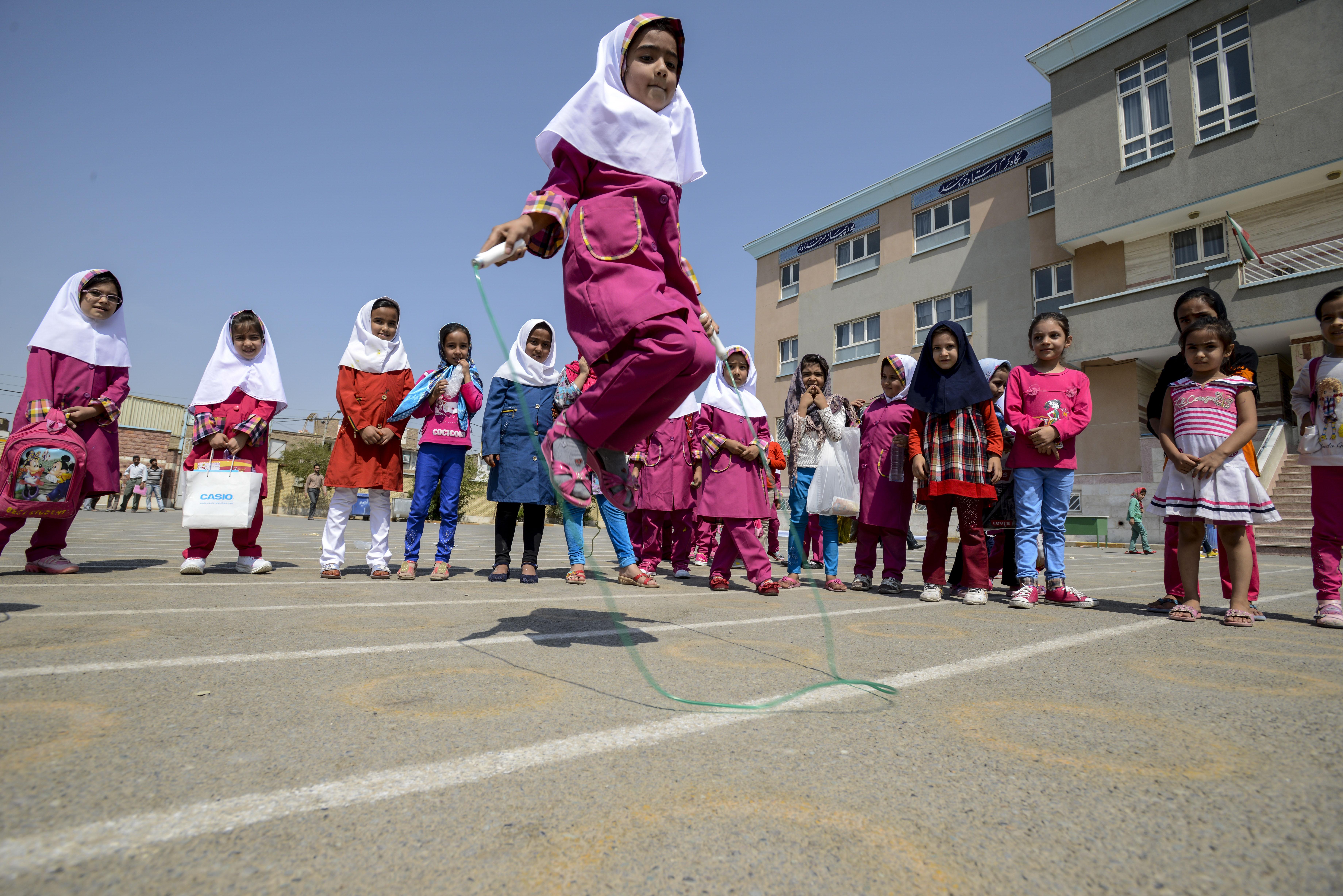 A girl jumps high over a skipping rope while others watch around. 