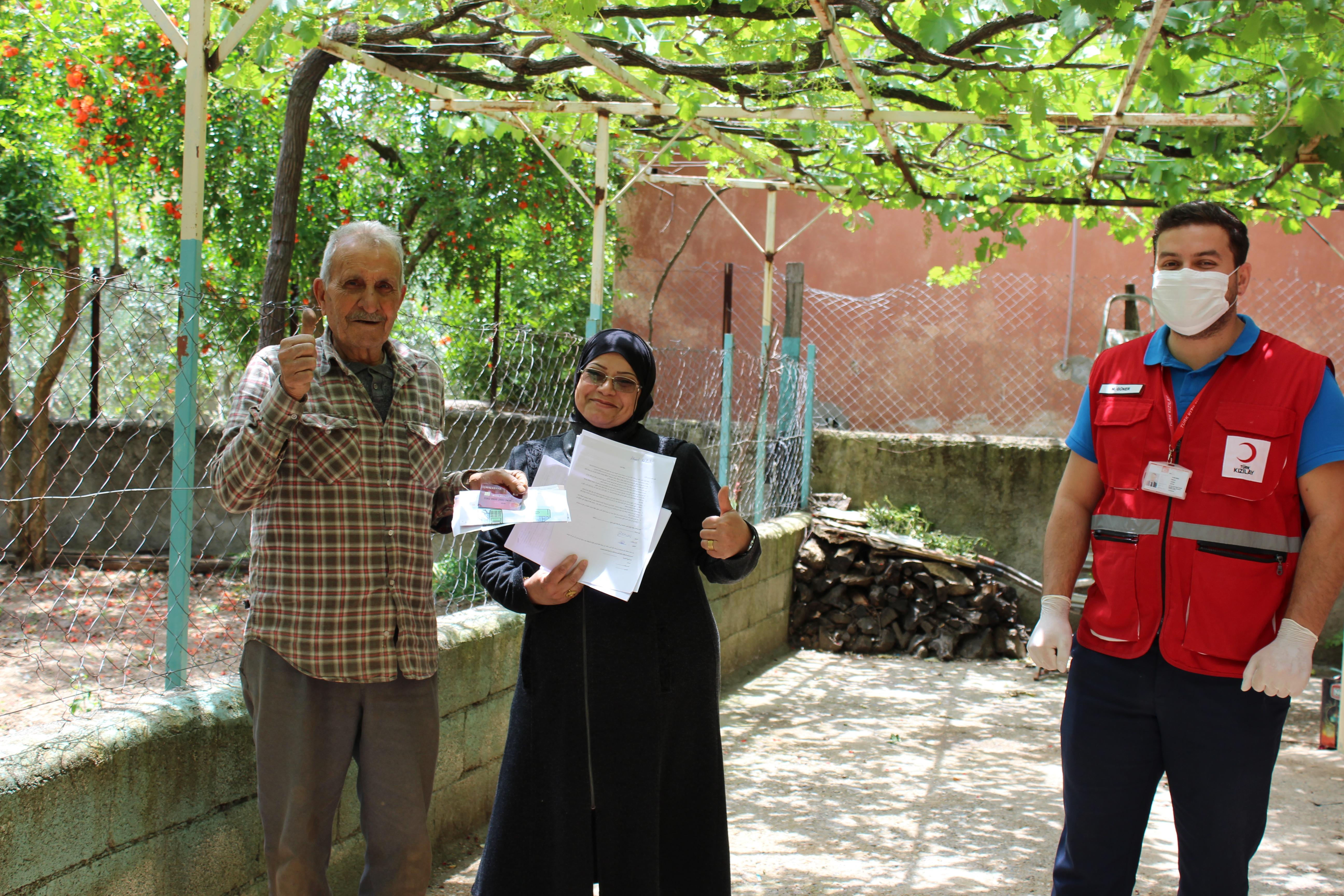 Two people stand on the left with their cards respecting the distance with a man from the red crescent wearing globes and a mask