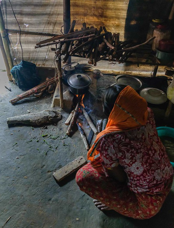 Woman seated on the floor in front of a cooker with firewood.
