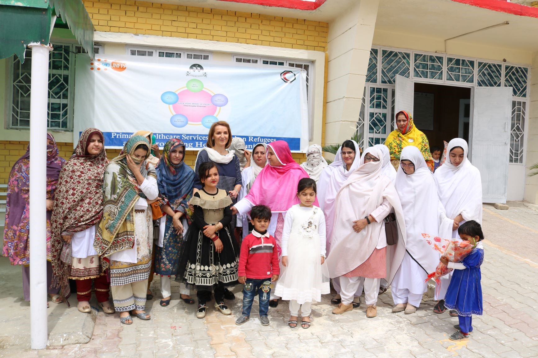 A group od women and children stand in front of a healthcare facility