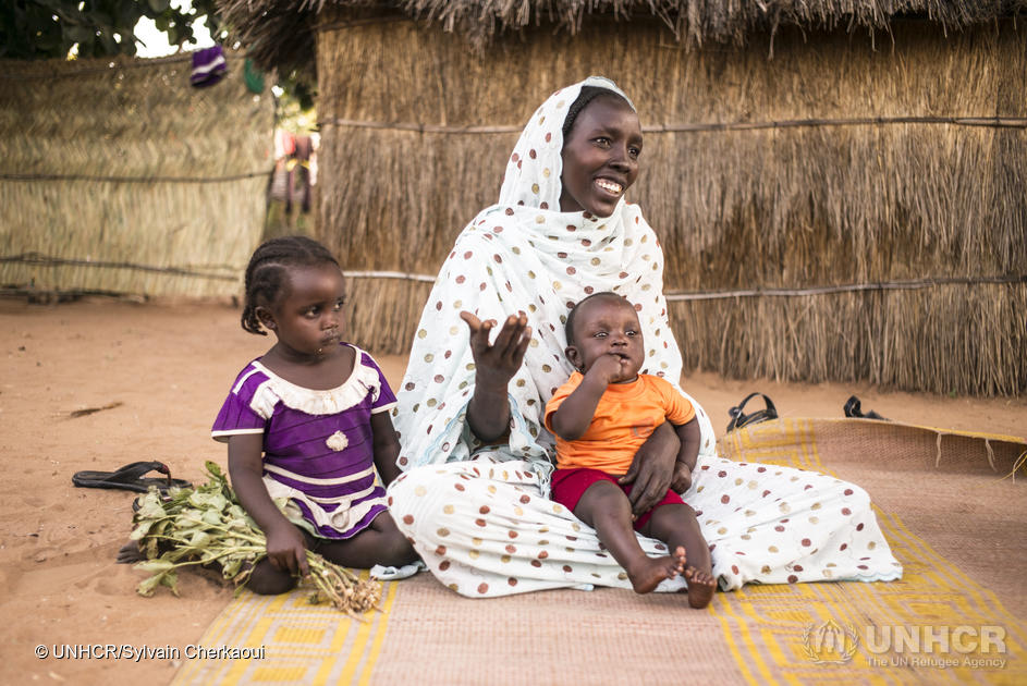 A woman sits with a child on her knees and one beside her