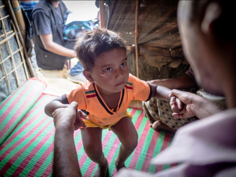 A disabled boy holding an adults hands and standing up