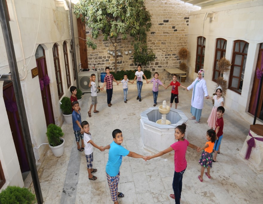 A group of children hold hands in a circle around a fountain 