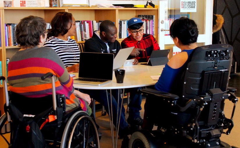 A group of people sitting together at a table, some are in wheelchairs.