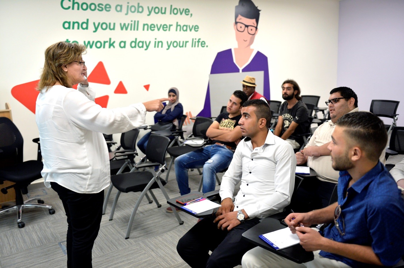 People seated listening to a woman talking in front of them. 