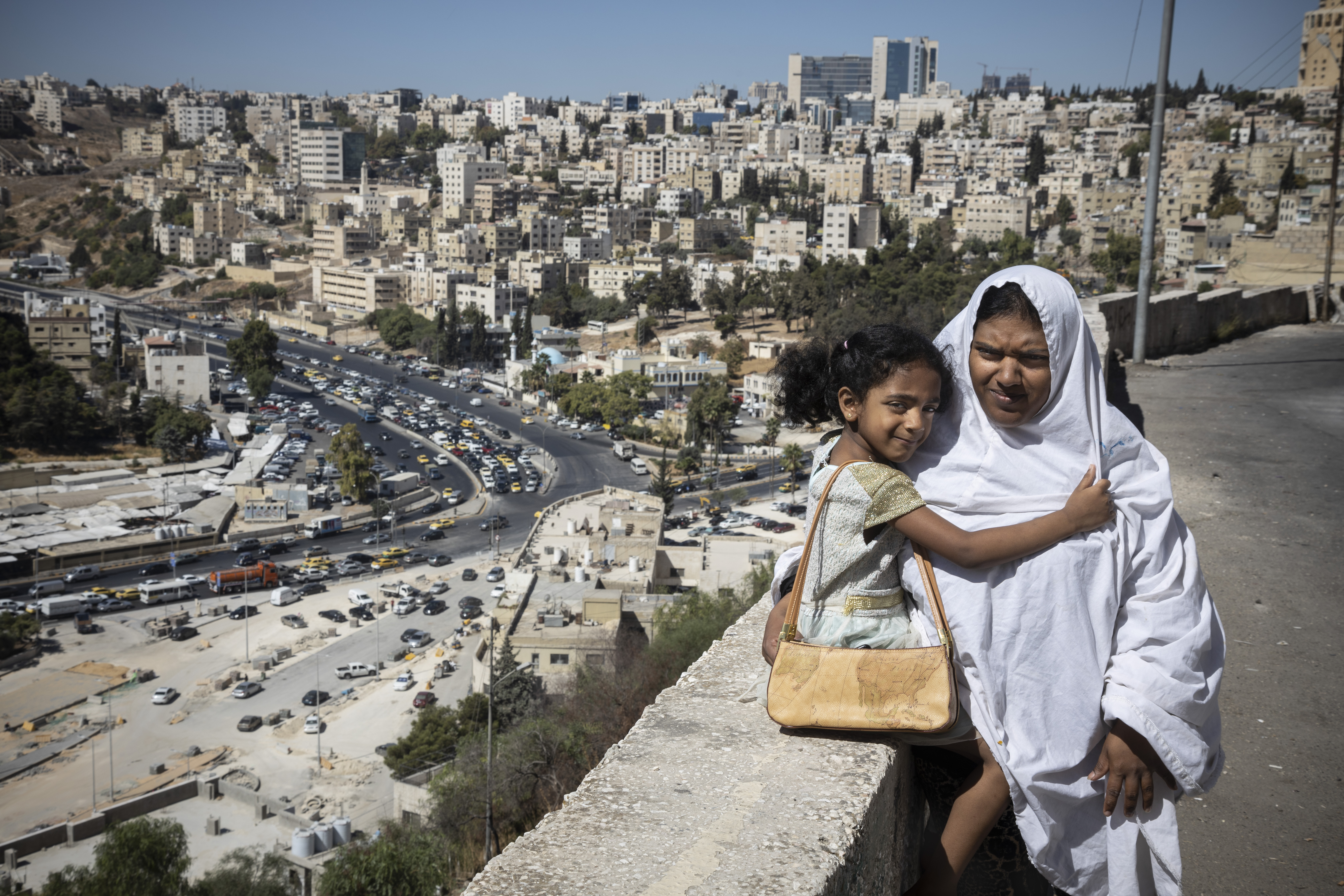 A lady and girl sit on a wall overlooking a city scape.