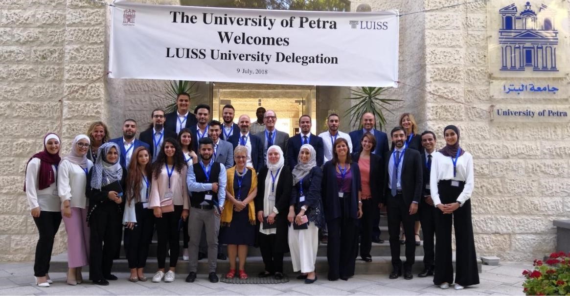 A group of people looking at the camera underneath a sign that says "The University of Petra Welcomes Luiss University Delegation 9 july 2018"