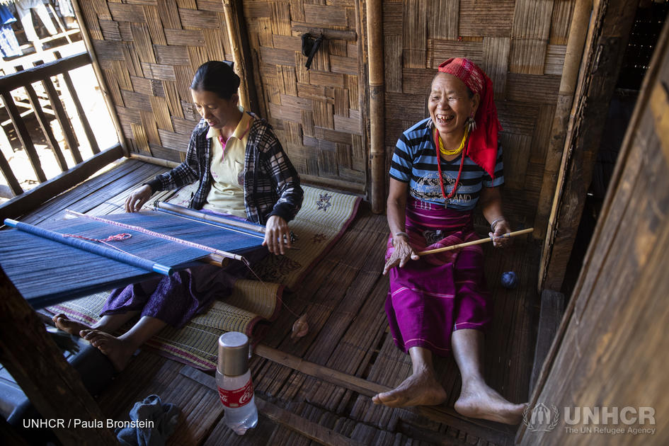 Two women sit together weaving