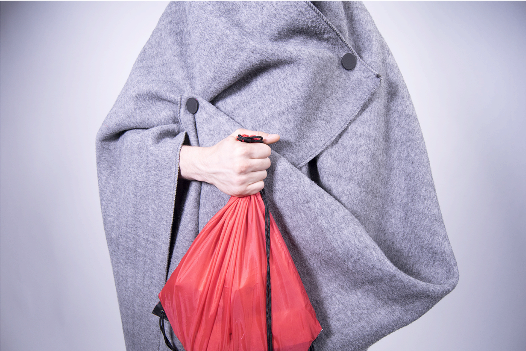 Torso of a person wearing an adapted UNHCR blanket and holding a red bag