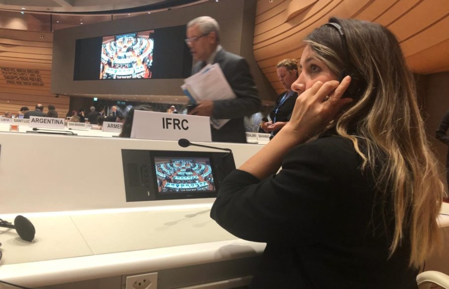 A woman wearing headphones sits behind an IFRC name tag in an assembly hall