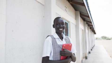 Kenya. Mary standing outside school holding a tablet