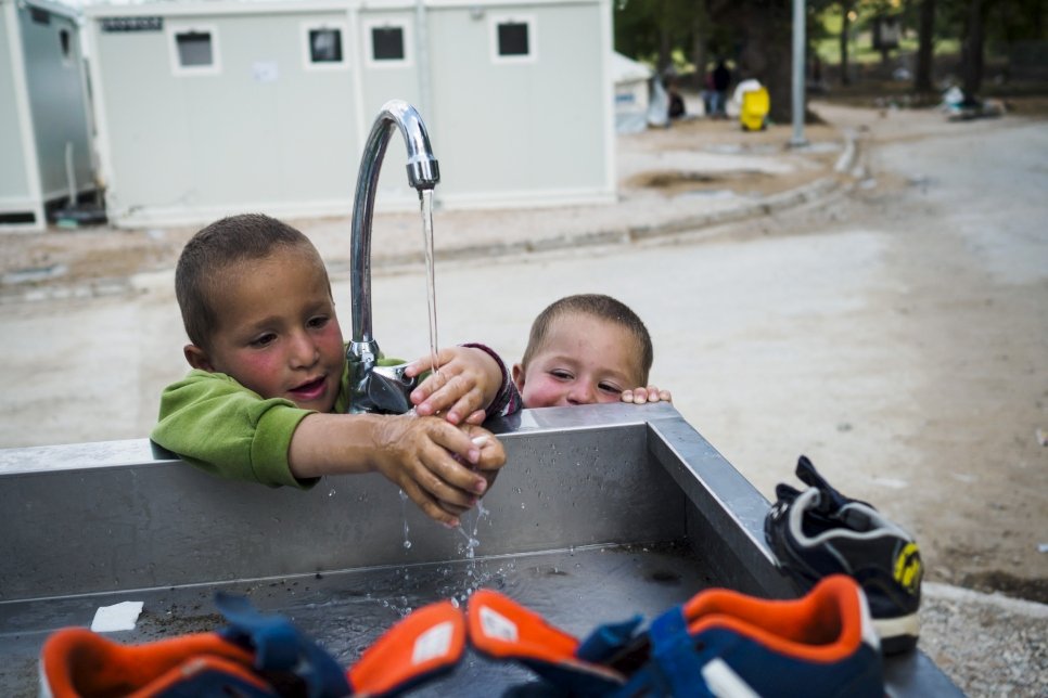 Two young brothers from Syria play with water at a WASH (Water, Sanitation and Hygiene) spot inside the new accommodation site at Lagkadikia.