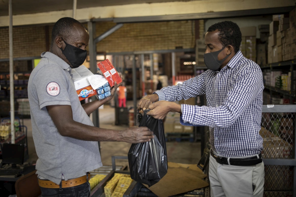 أمين شيخ (يمين) يسلم كيساً من المواد إلى أحد السكان الجنوب إفريقيين أثناء عملية توزيع الطعام في بريتوريا، جنوب إفريقيا.