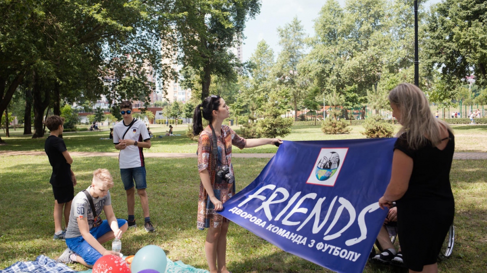 Valentyna Uvarova and Maryna Tolokova, who are internally displaced, hold a banner for Friends football team during a birthday party for Pavlo Soroka, son of Tetiana Baransova. The team fights discrimination in sports.