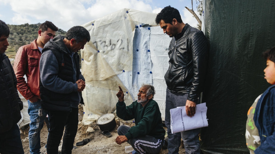Sardar (izq.) habla con Abdul What Qadiri (sentado), un solicitante de asilo afgano de 65 años que tiene cáncer, en el centro de recepción e identificación de Moira, en la isla de Lesbos.