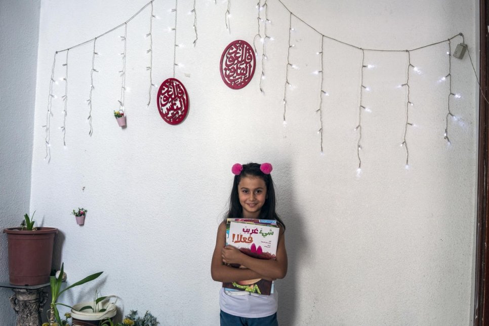 اللاجئة السورية راما، البالغة من العمر ثماني سنوات، تحمل قصة قرأتها من قبل إحدى سفراء برنامج "نحن نحب القراءة" في عمان.