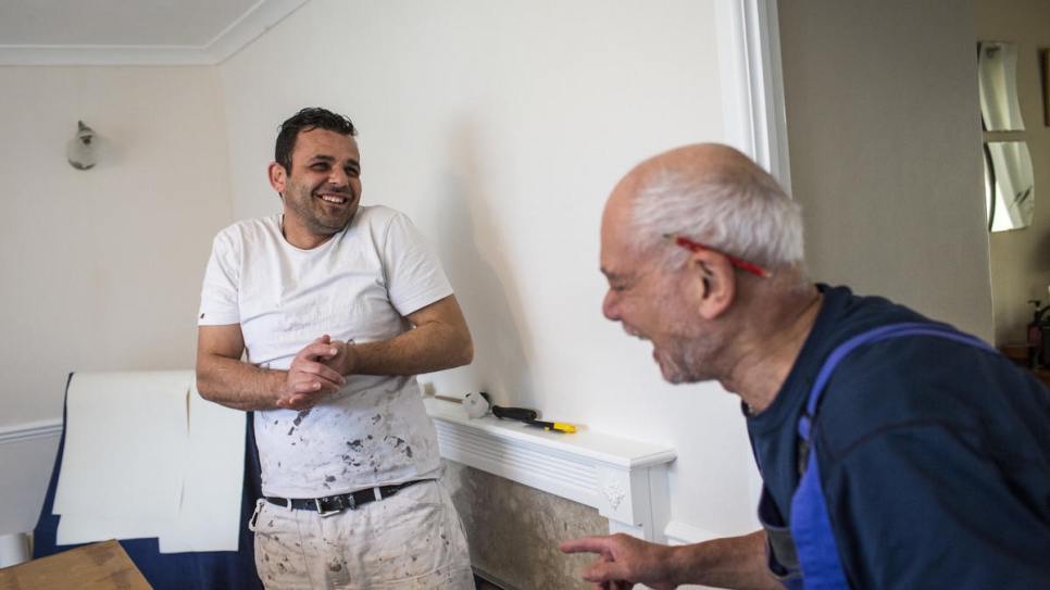 Hani Arnout (left), 34, shares a joke with local painter and decorator Trevor Leahong as they paint a house together in Ottery St Mary, Devon. Trevor gives Hani work whenever he can.