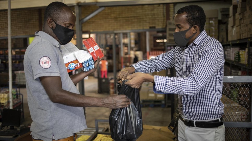 Amin Sheikh (à droite) remet un sac de marchandises à un Sud-Africain en difficulté lors d'une distribution de nourriture à Pretoria, en Afrique du Sud. 