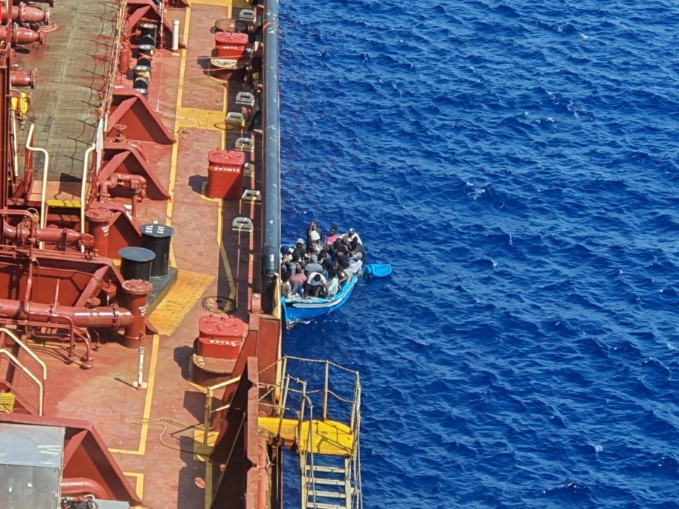 Malta. Migrants sit in a boat alongside the Maersk Etienne tanker