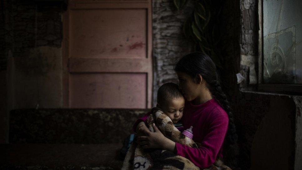 Naamat feeds her youngest brother Ibrahim a bottle of formula milk.