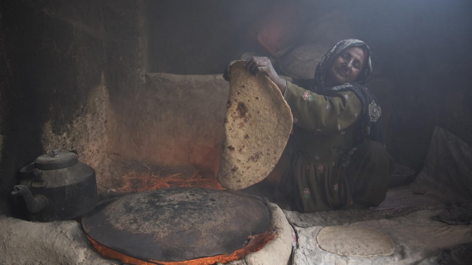 Sardar Bibi cooks traditional Afghan bread in the one-room shelter she shares with 21 members of her family. They will soon move into their new, larger home (4 February, 2020).