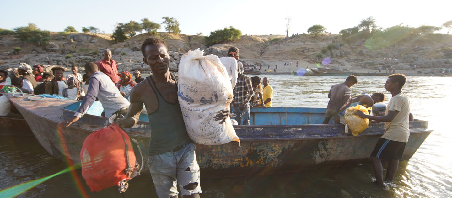 Ethiopische vluchtelingen, op de vlucht voor conflict in de Tigrayregio van het land, halen overlevingsmateriaal van een boot op de Tekezerivier nadat ze de grens zijn overgestoken naar Hamdayet, Soedan. © UNHCR/Hazim Elhag