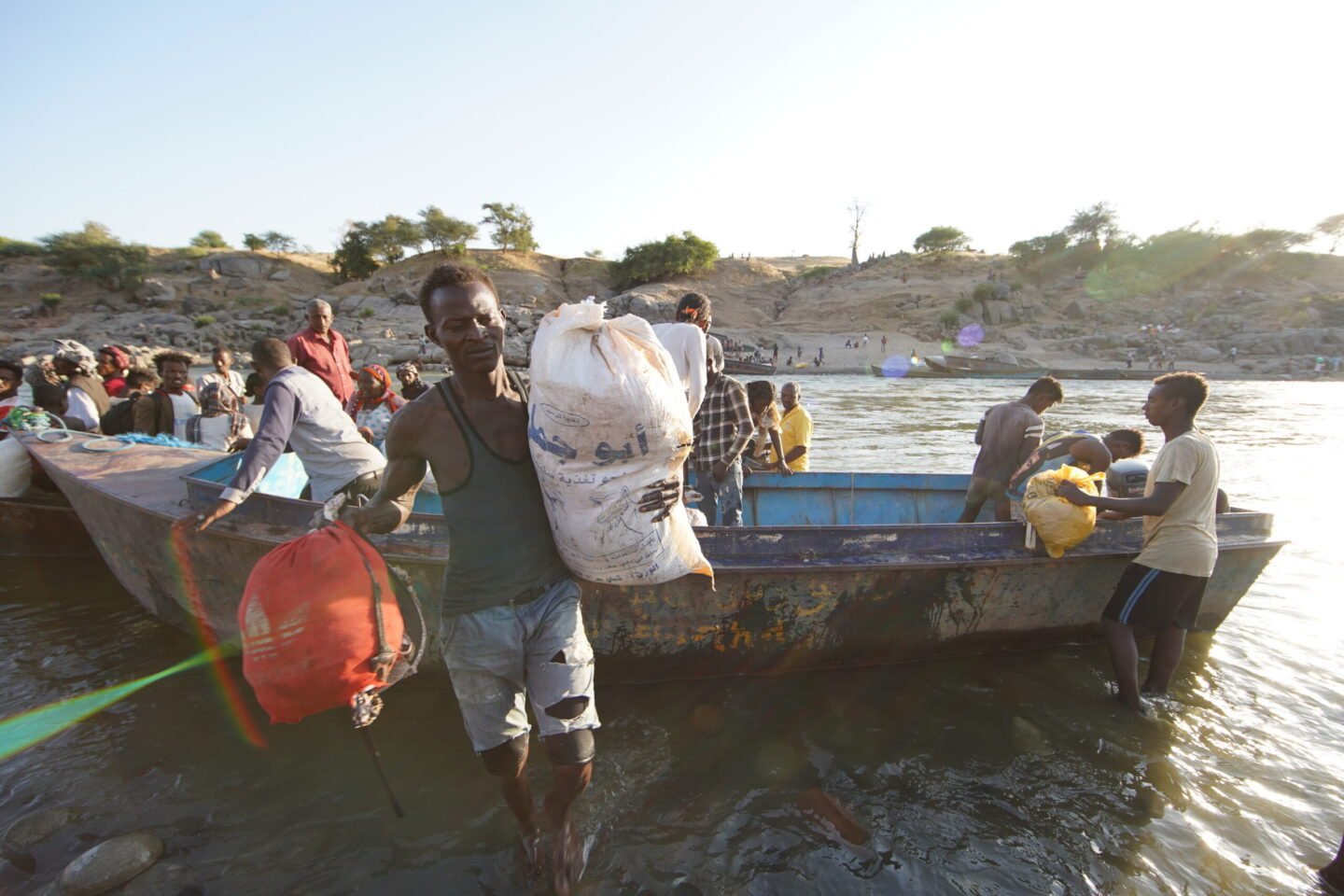 Ethiopische vluchtelingen, op de vlucht voor conflict in de Tigrayregio van het land, halen overlevingsmateriaal van een boot op de Tekezerivier nadat ze de grens zijn overgestoken naar Hamdayet, Soedan. © UNHCR/Hazim Elhag
