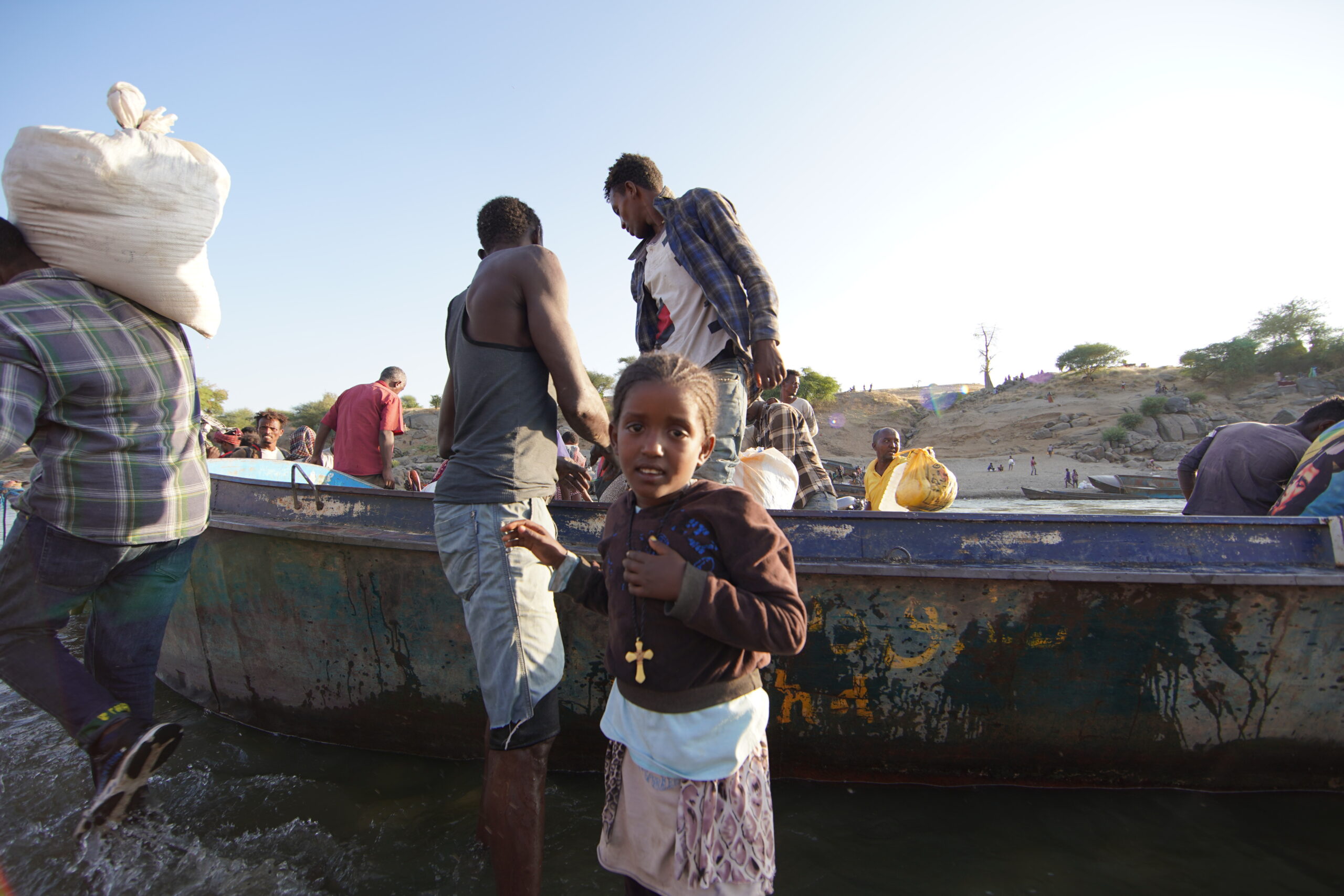 Ethiopische vluchtelingen, op de vlucht voor conflict in de Tigrayregio van het land, halen overlevingsmateriaal van een boot op de Tekezerivier nadat ze de grens zijn overgestoken naar Hamdayet, Soedan. © UNHCR/Hazim Elhag