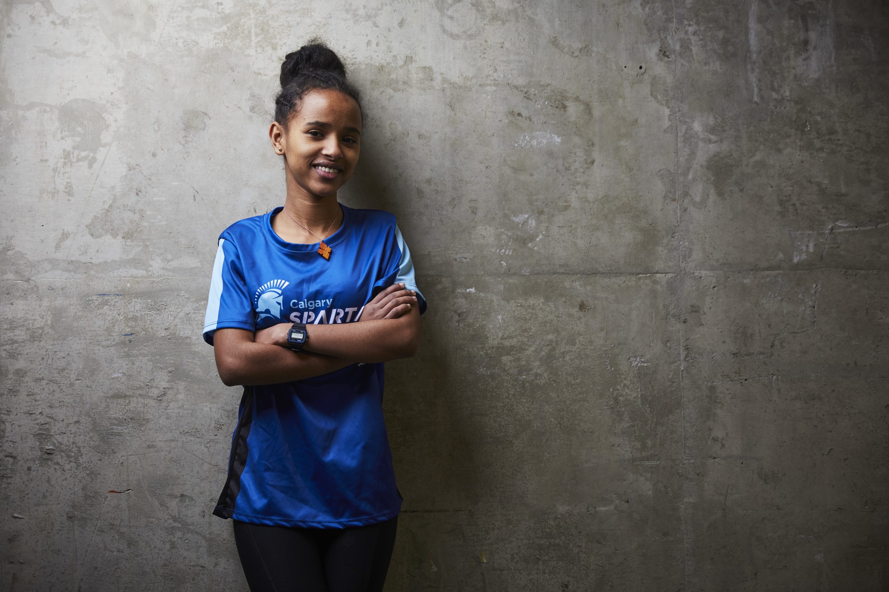 A young woman leans up against a concrete wall with her arms crossed over her chest.