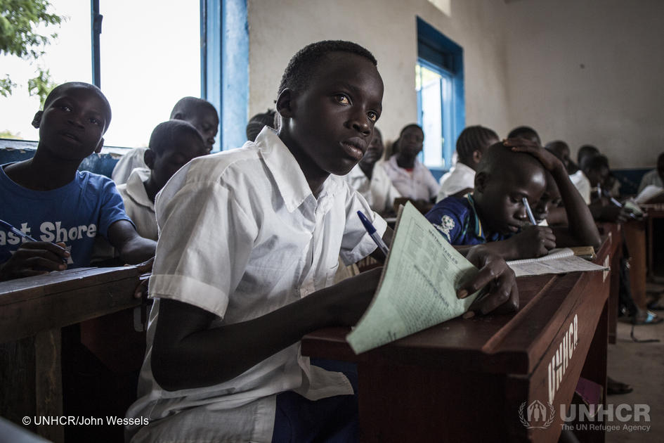 Young refugee from South Sudan striving for an education sits in a classroom taking notes surrounded by his classmates