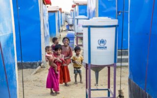 Rohingya children playing among blue tents and water cylinders